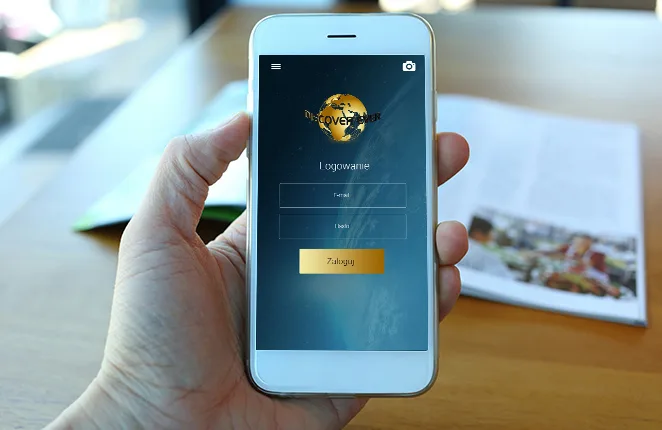 Smartfon z ekranem logowania aplikacji Discover Ever nad otwartym drukowanym magazynem