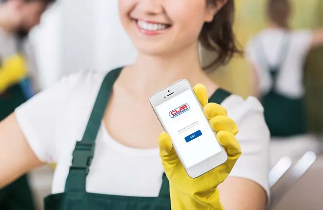Pracownica firmy sprzątającej w żółtych rękawicach pokazuje smartfon z aplikacją CLAR System