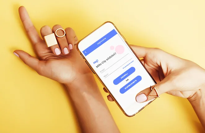 Dłoń z pomalowanymi paznokciami i smartfon z ekranem logowania aplikacji Nails Room