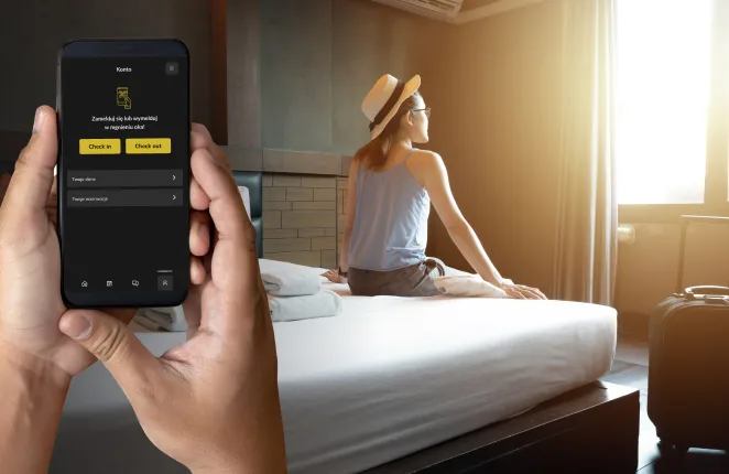 Dłonie trzymające smartfon z aplikacją hotelową, w tle gość w pokoju hotelowym
